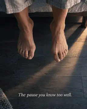 Bare feet hesitating at the edge of a bed on a hardwood floor — the familiar pause before the first painful step
